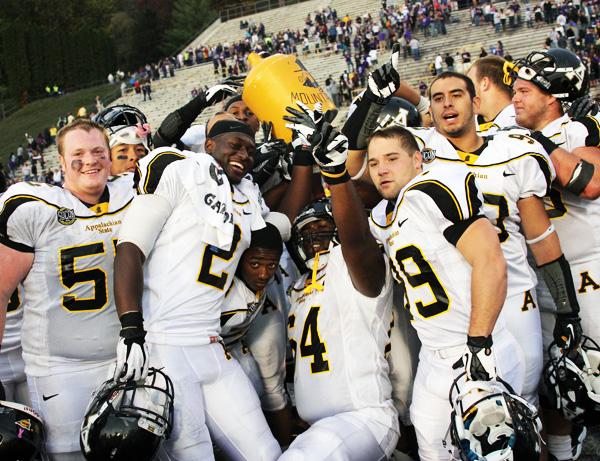 Members of Mountaineer offensive line celebrate their win with the 'Old Mountain Jug' on the field Saturday. The team pounced the Catamounts for a 38-27 win. Paul Heckert | The Appalachian 