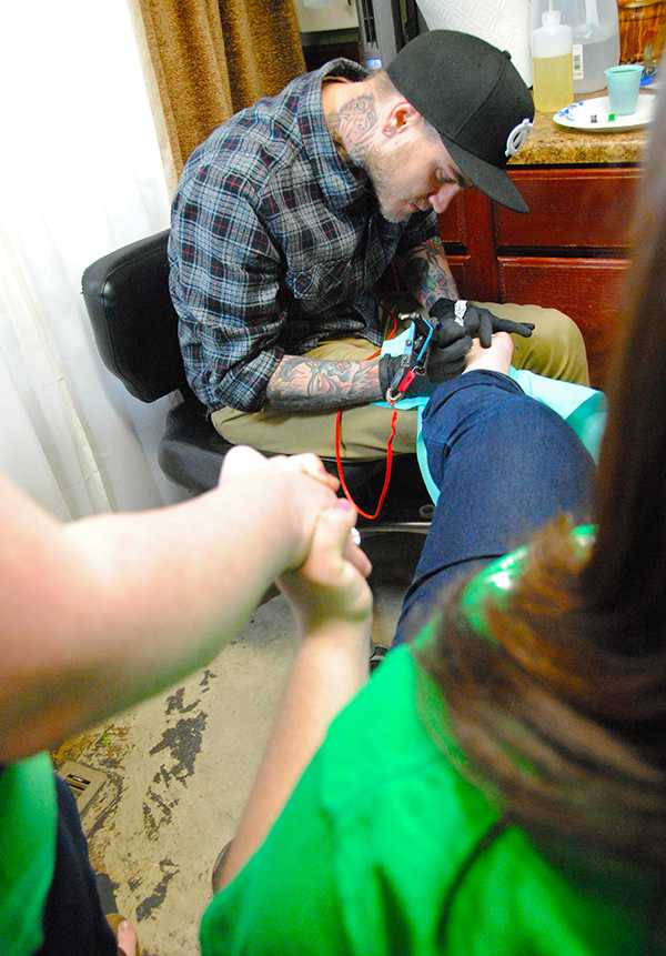 Two sisters, alumna Amanda Prendiville and junior psychology major Katrina Prendiville hold hands while former Speakeasy Tattoo artist Justin Essing tattoos a shamrock onto Katrina’s foot at last year's St. Patrick's Day Tattoos for Schools fundraiser. This year's fundraiser will be held on Sunday, March 17th beginning at 7 a.m.  Olivia Wilkes  |  The Appalachian 